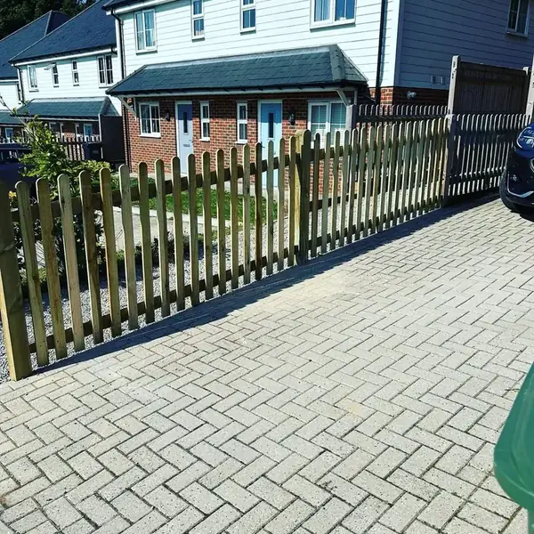 Round-top timber picket fence bordering a block-paved driveway