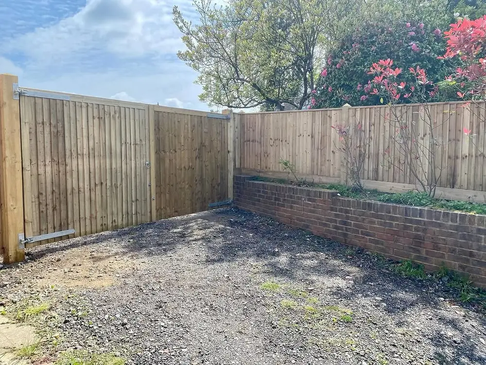 Closeboard fence above a low brick retaining wall beside a gravel drive