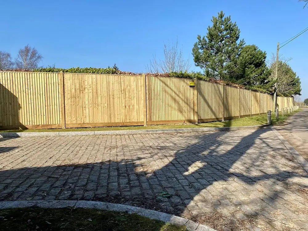 Closeboard fence along a block-paved driveway with trees behind