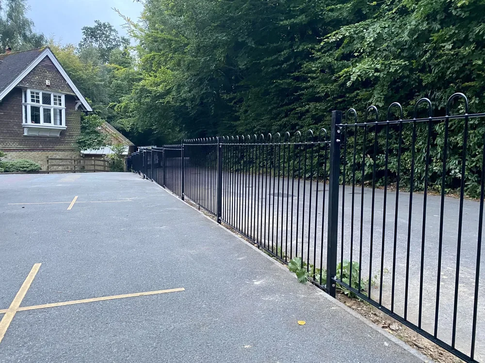 Run of black bow-top railings along a school car park