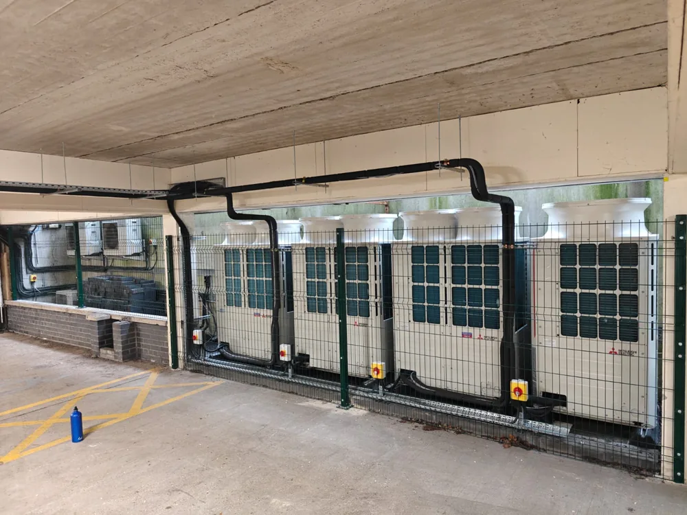 Green mesh fencing enclosing air-conditioning plant in a car park undercroft