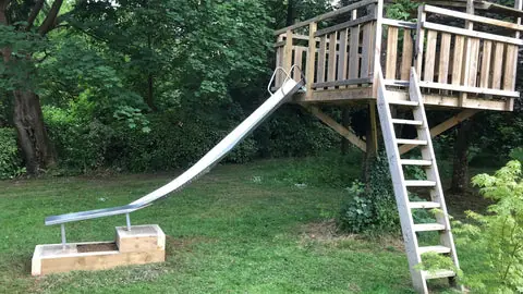 Raised timber play platform with a slide and steps in a garden