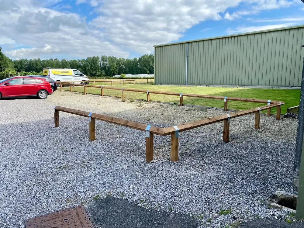 Knee-rail fencing edging a gravelled parking area beside an agricultural building