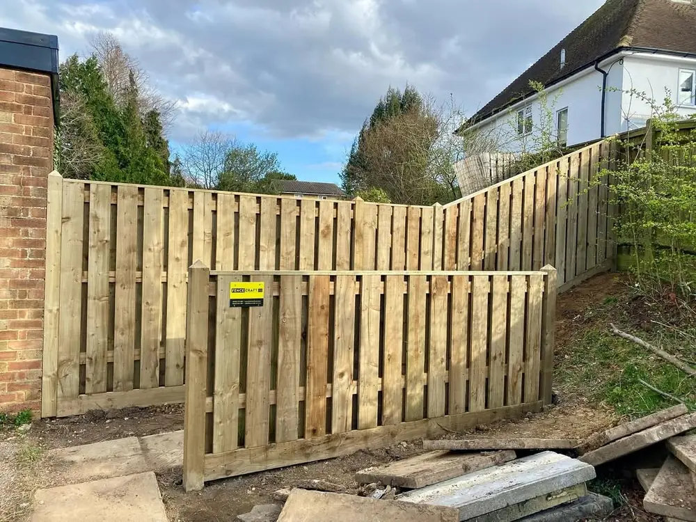 Vertical hit and miss fencing with a gate, part-built beside a house