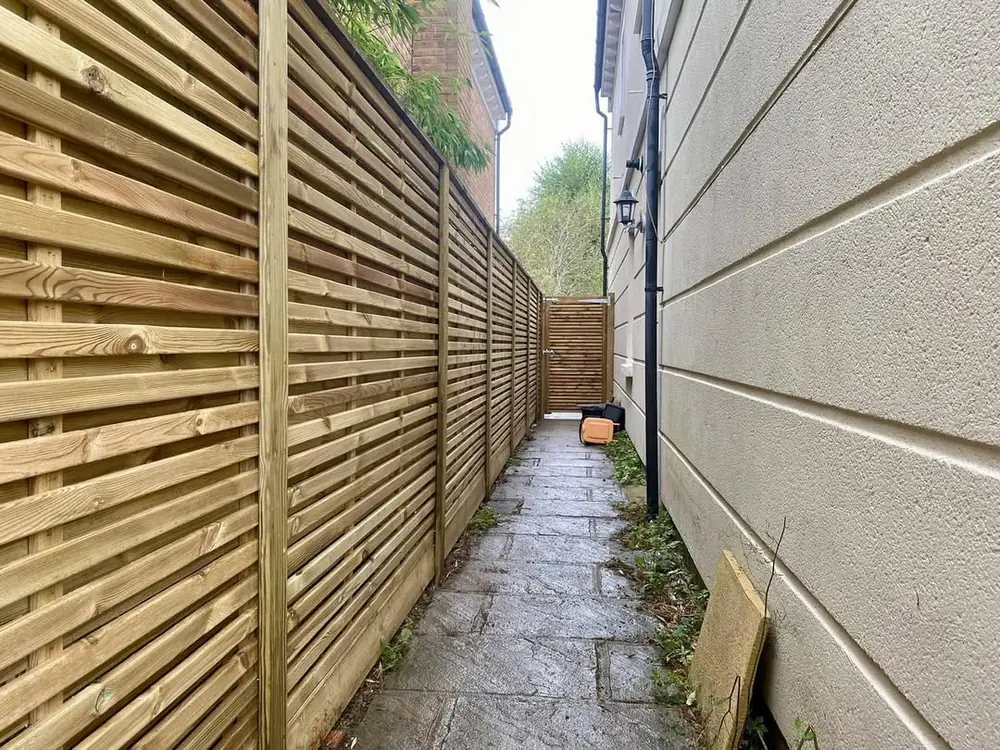Venetian slatted panel fencing along a narrow side passage