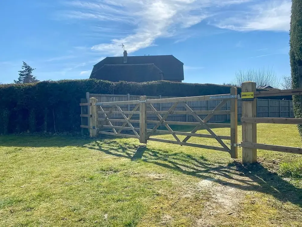 Five-bar timber field gate set into post and rail fencing beside a hedge