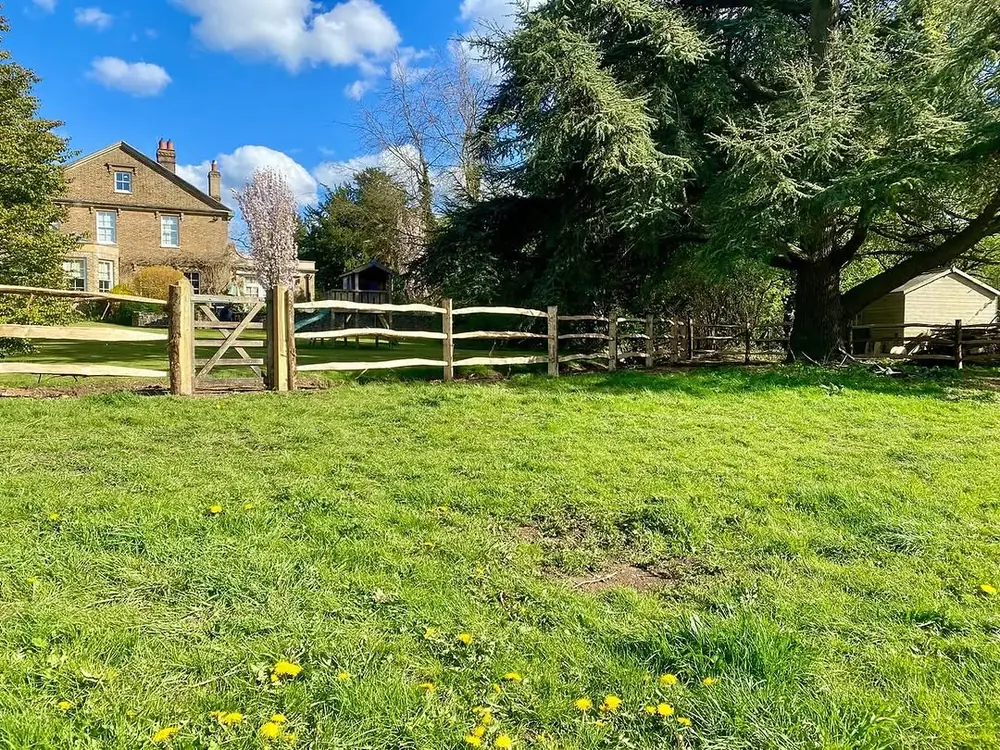 Post and rail fencing and a timber gate across a grass paddock in front of a farmhouse