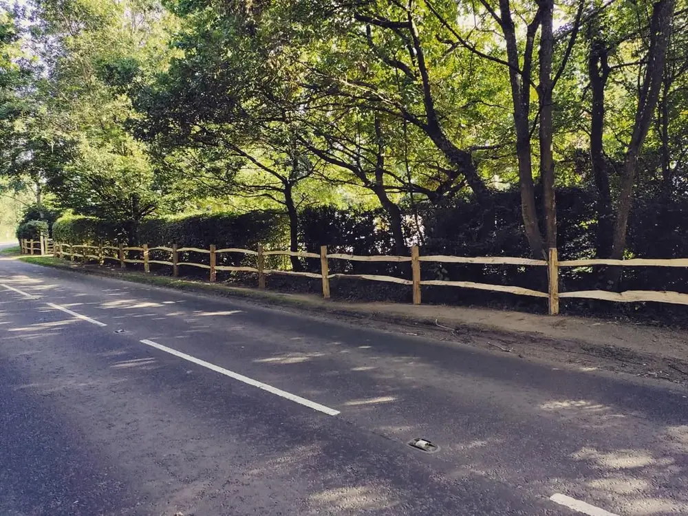 Post and rail fencing running along a tree-lined roadside verge